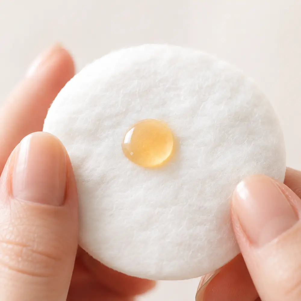 A golden drop of argan oil on a white cotton pad held between two fingers