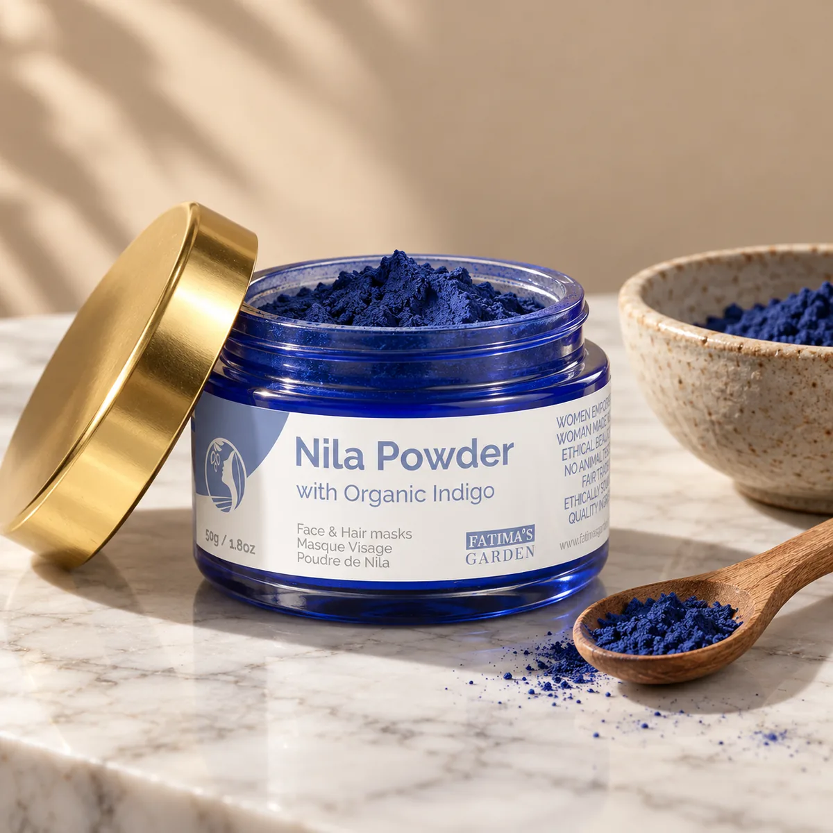 The Fatima’s Garden 50 g nila powder jar, open on marble, a wooden spoon of deep blue indigo powder beside it